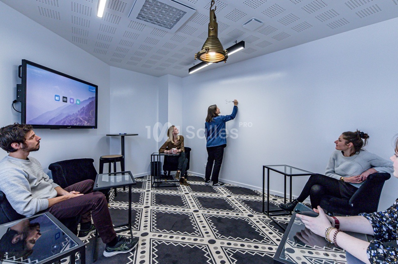 Une personne écrit sur un tableau blanc dans une salle de réunion, entourée de quatre autres personnes assises.