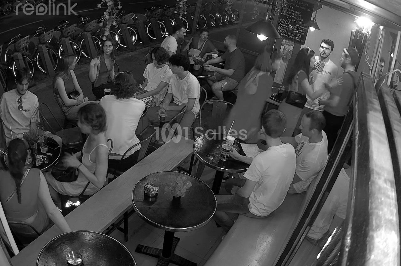Des personnes discutent et partagent un moment convivial dans un bar animé, capturé en noir et blanc.