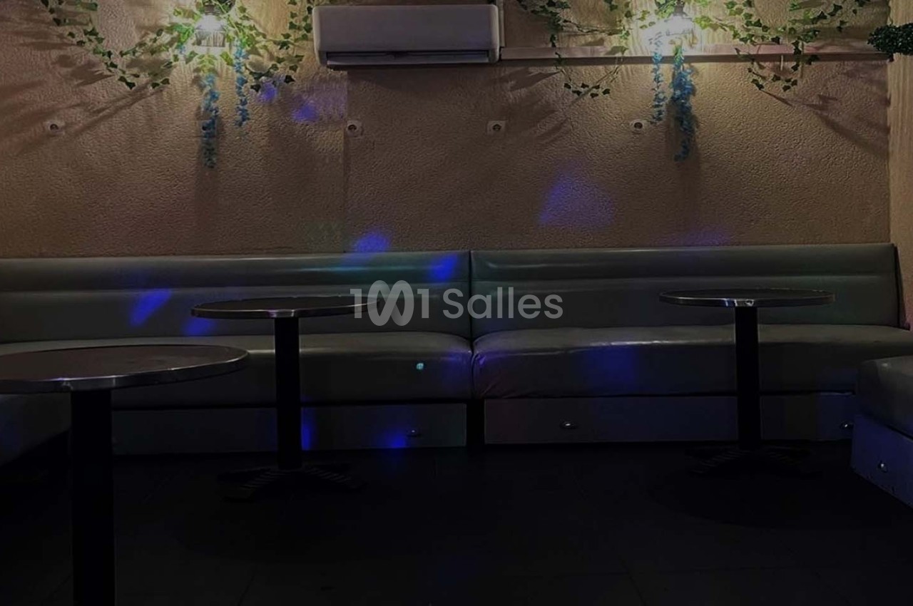 Banquettes grises et tables rondes dans une pièce sombre avec éclairage tamisé et décorations végétales murales.