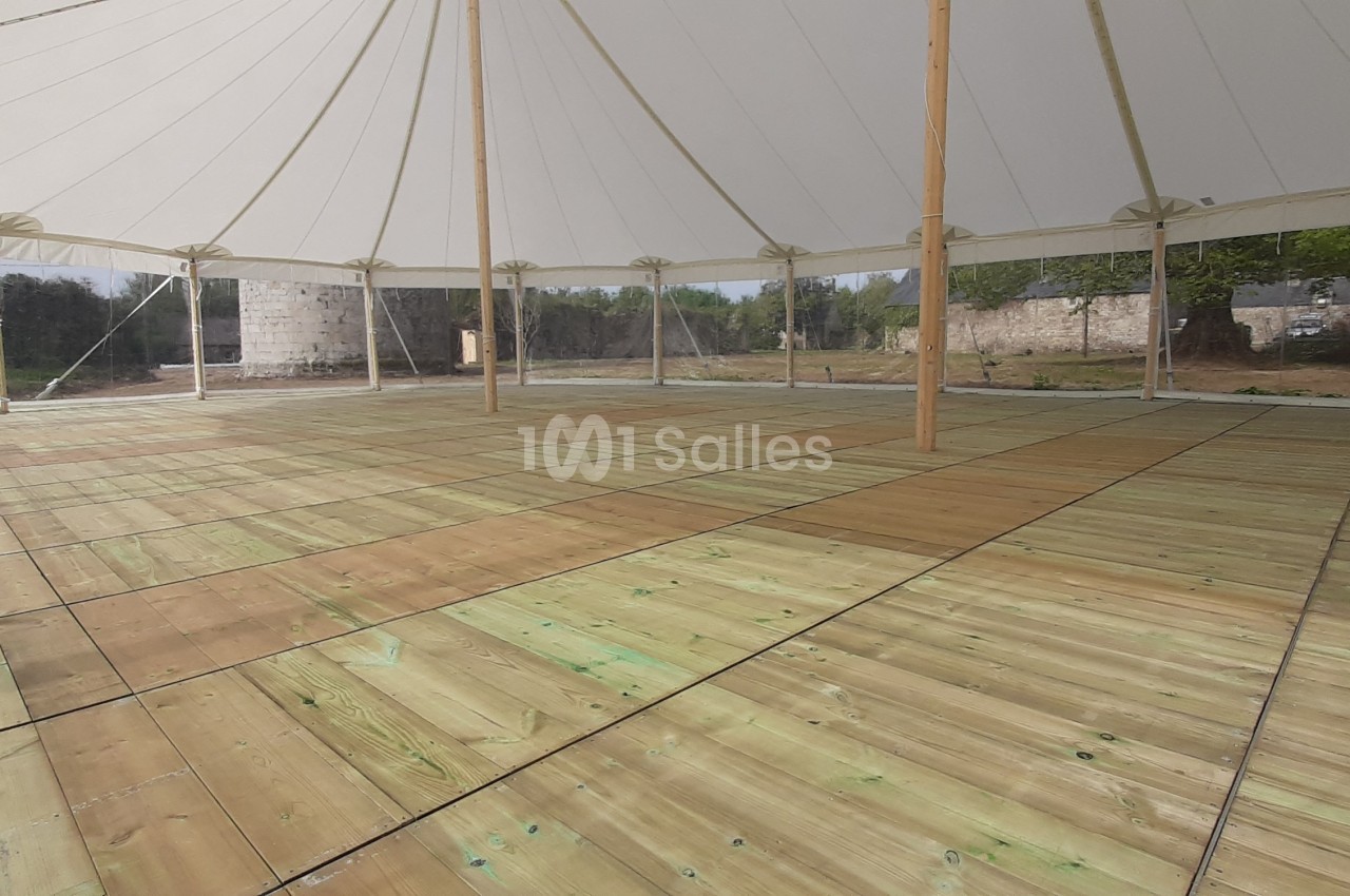 Intérieur d'une tente avec un sol en bois clair, entourée de parois transparentes et située dans un espace extérieur…