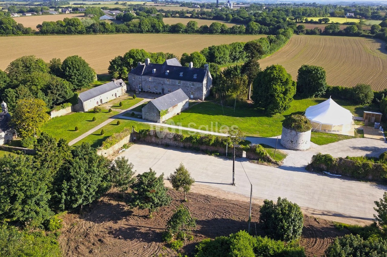 Vue aérienne d'un domaine rural avec bâtiments en pierre, cour centrale, tour ronde et champs environnants.