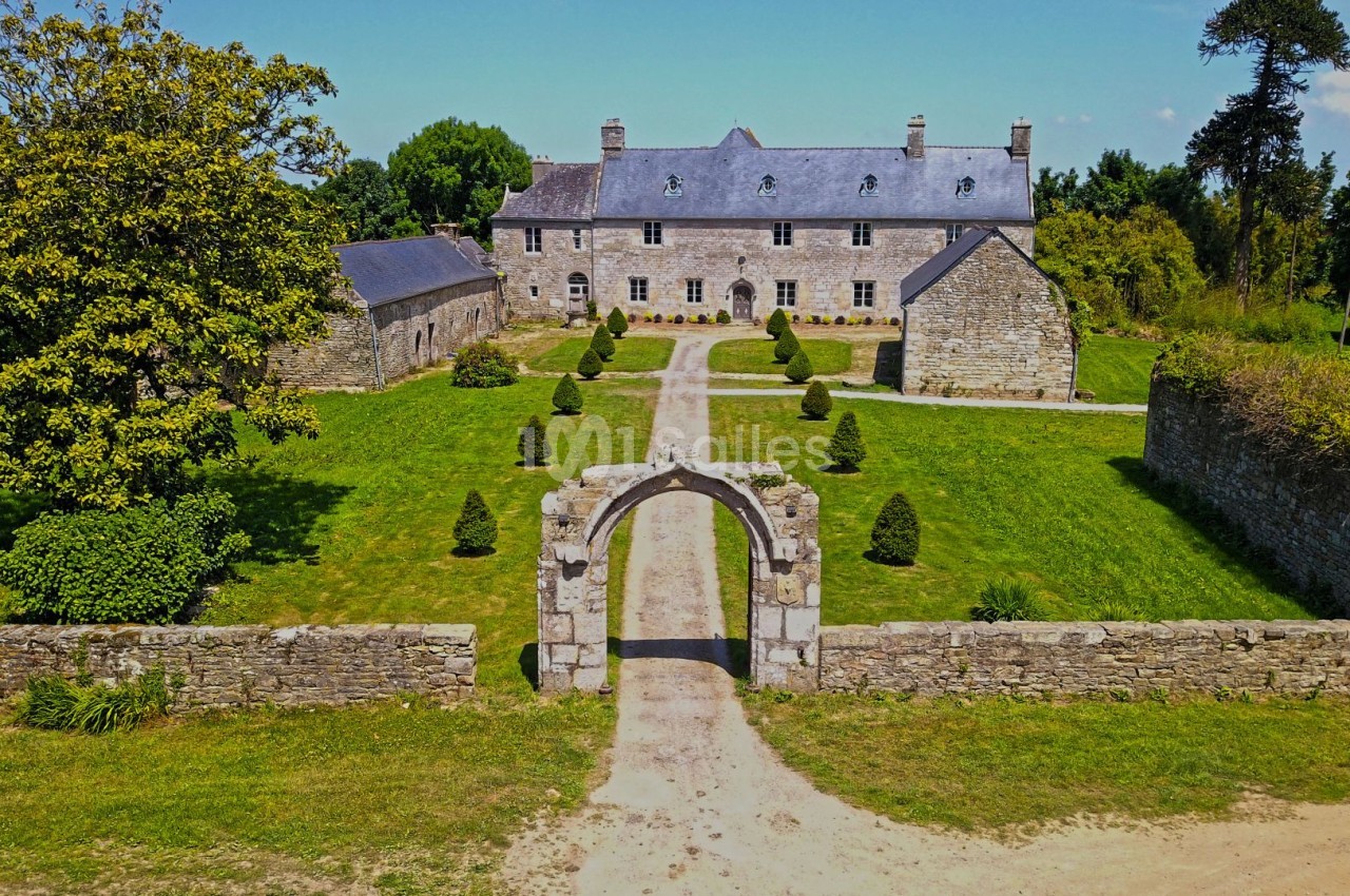 Vue aérienne d'un manoir en pierre entouré de jardins, d'une allée centrale et de murs en pierre.