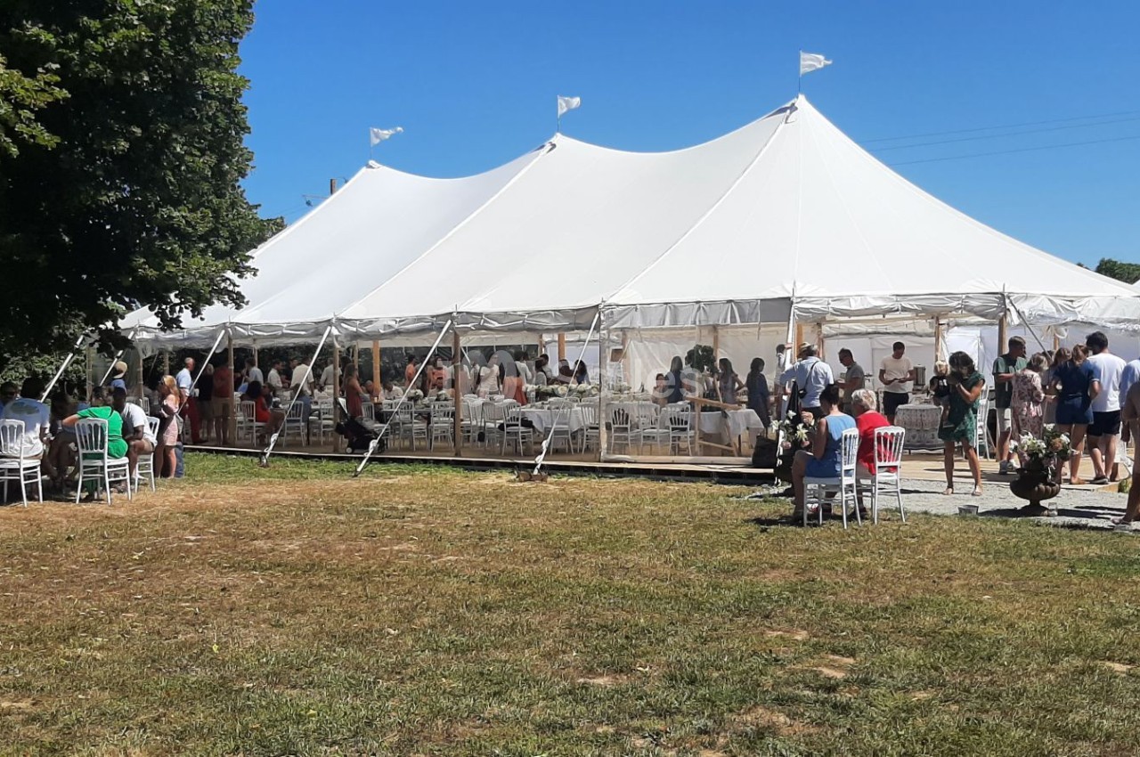 Grande tente blanche installée en extérieur, entourée de personnes debout et assises lors d'un événement par temps…