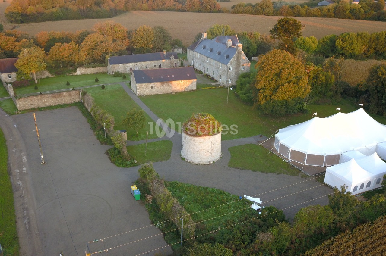 Vue aérienne d'un domaine rural avec bâtiments en pierre, une tente blanche et des espaces verts environnants.