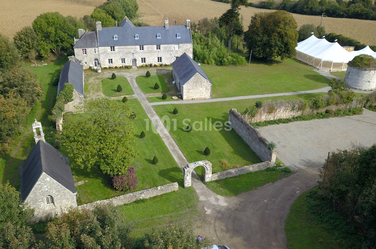 Vue aérienne d'un manoir en pierre entouré de jardins, d'annexes, d'une tente blanche et de champs.