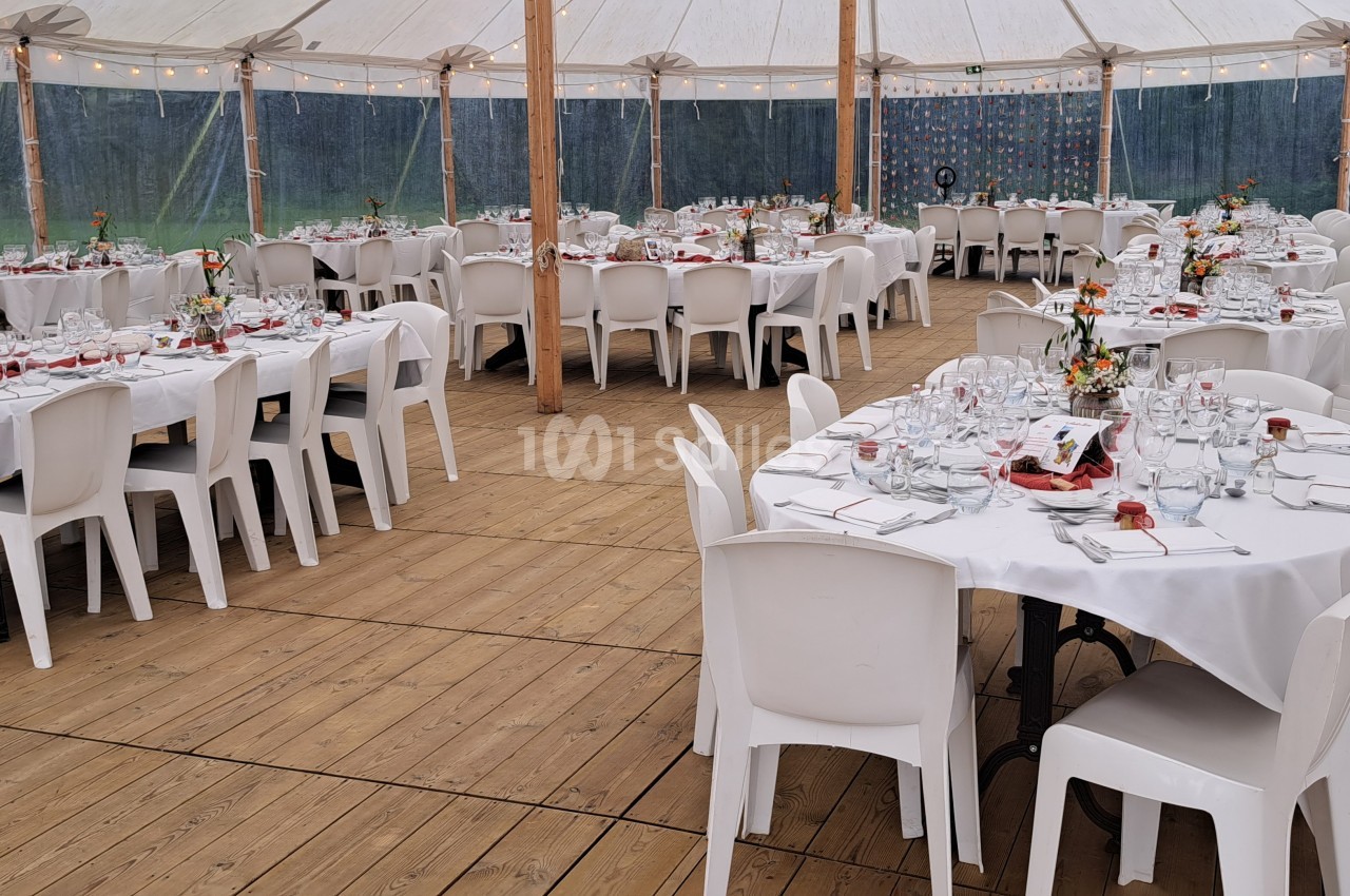 Salle de réception sous chapiteau avec tables rondes et rectangulaires dressées pour un événement.