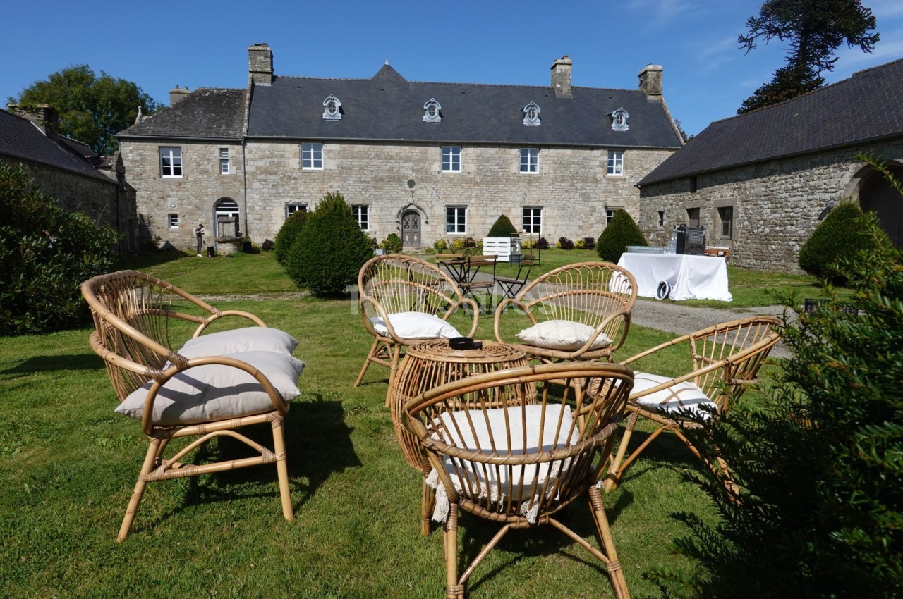 Fauteuils en rotin disposés sur une pelouse devant une grande bâtisse en pierre sous un ciel bleu.
