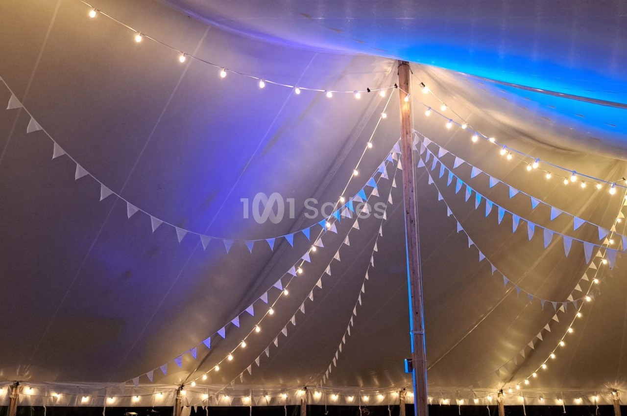 Guirlandes lumineuses suspendues sous une tente blanche avec des fanions triangulaires et un éclairage bleu.