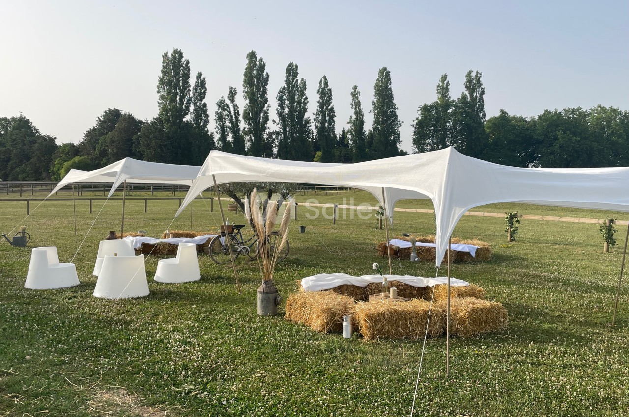Tentes blanches montées sur une pelouse avec des bottes de paille disposées en sièges autour de tables basses.