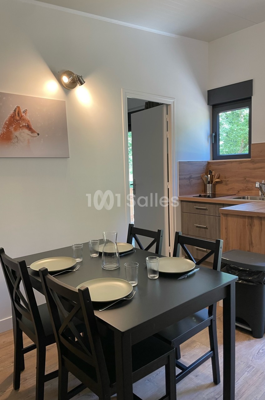 Table noire dressée pour quatre personnes dans une cuisine moderne avec meubles en bois et tableau mural représentant un…