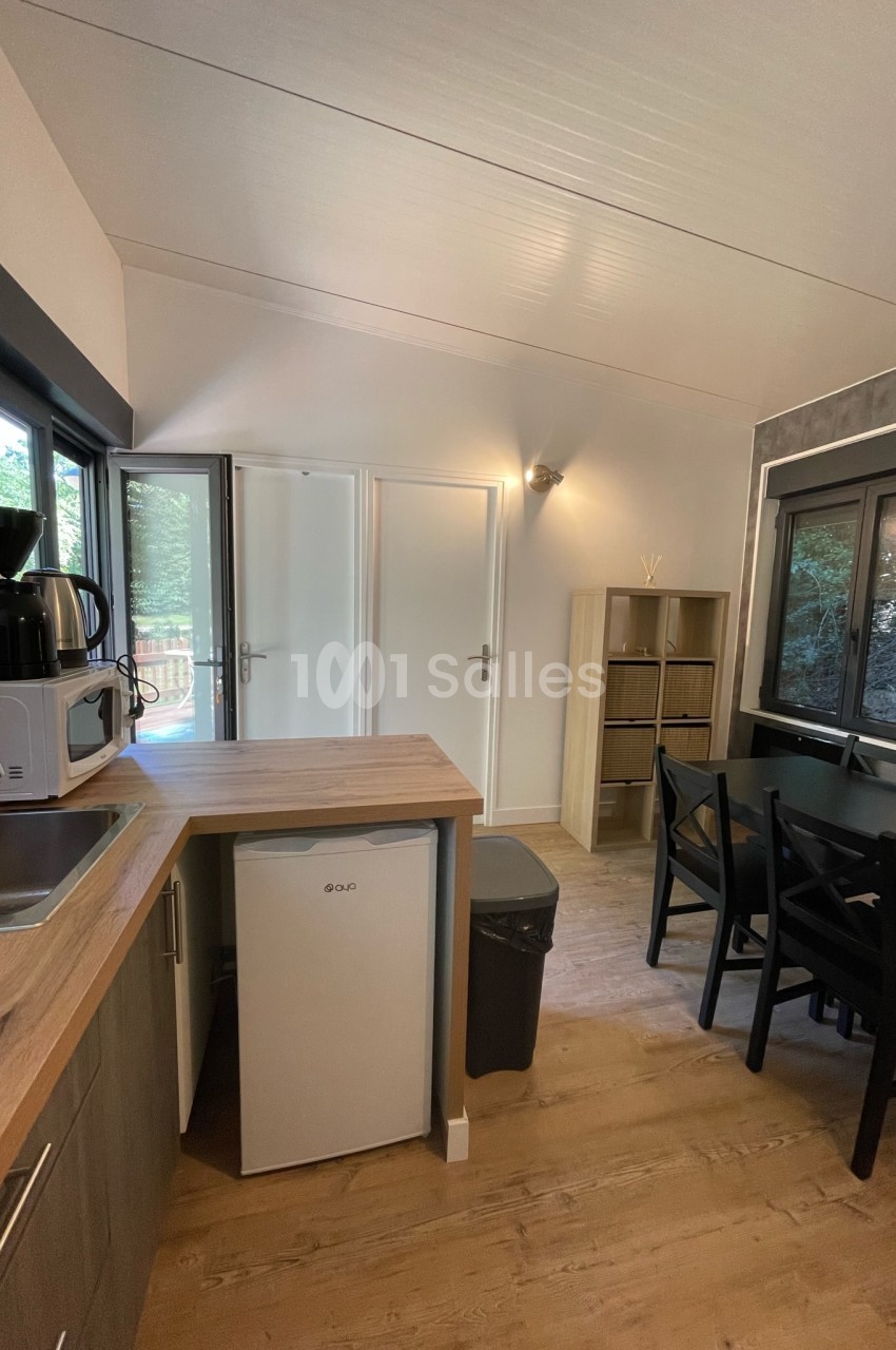 Cuisine compacte avec plan de travail en bois, réfrigérateur, micro-ondes, cafetière et table à manger près d'une fenêtre.