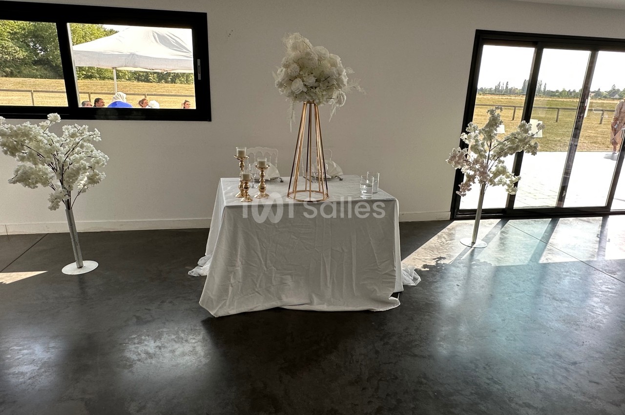 Table décorée avec une nappe blanche, des chandeliers dorés et un bouquet de fleurs blanches, dans une salle lumineuse.