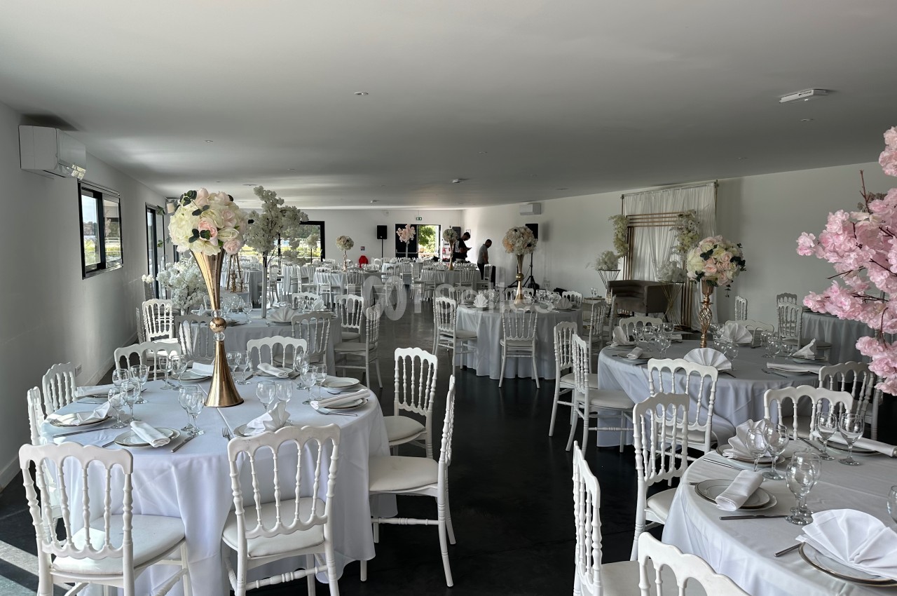 Salle de réception élégamment décorée avec des tables rondes, nappes blanches et centres de table fleuris.