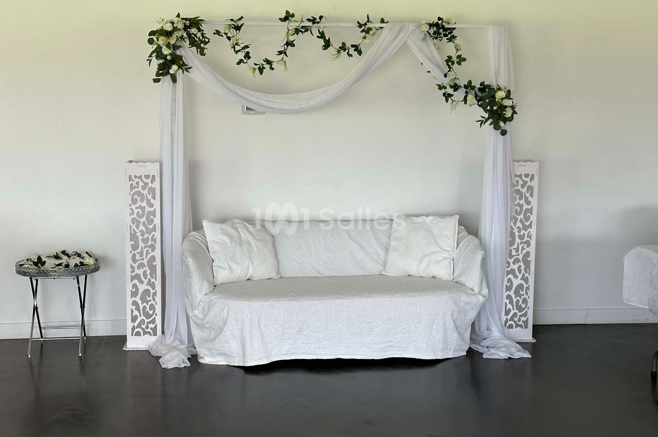 Canapé blanc décoré de drapés et de feuillages, encadré par deux colonnes ajourées dans une pièce lumineuse.