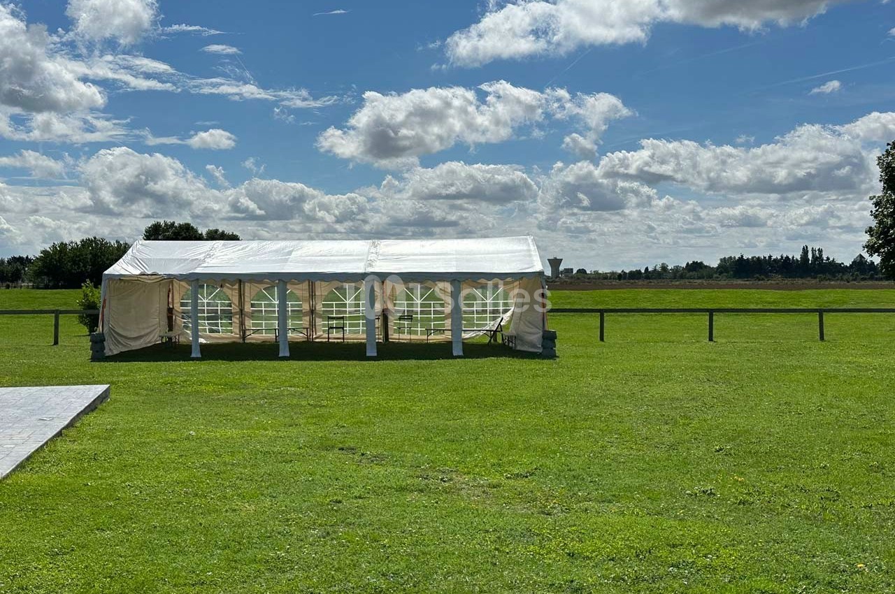 Tente blanche installée sur une pelouse verte sous un ciel partiellement nuageux.