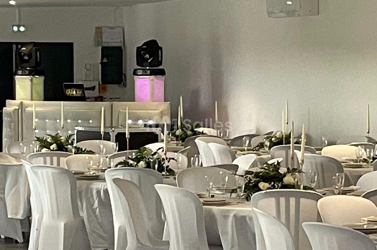 Salle de réception décorée avec des tables dressées, nappes blanches, chandeliers et compositions florales.