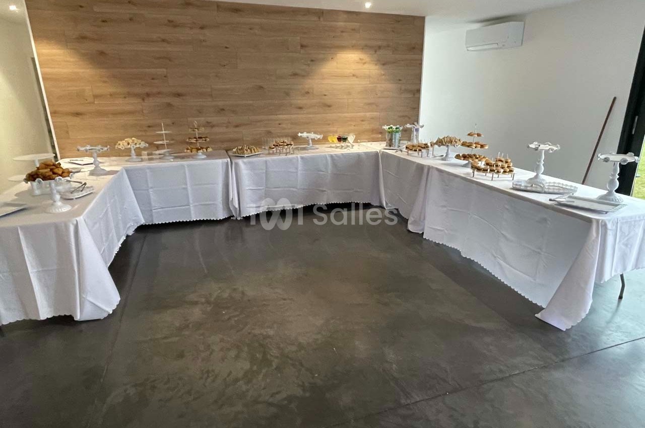 Tables dressées avec nappes blanches, disposées en U, présentant un buffet de desserts sur des présentoirs.
