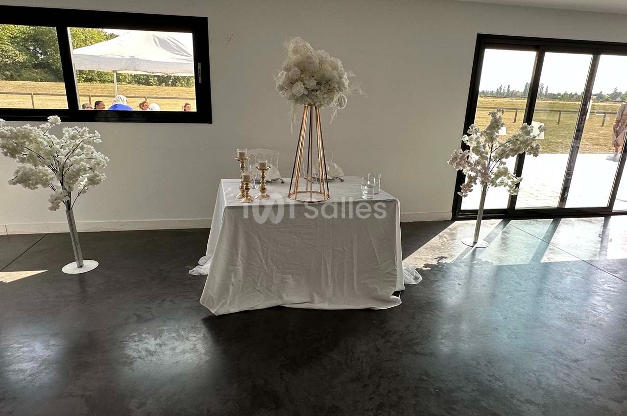 Table décorée avec une nappe blanche, des chandeliers dorés et un bouquet de fleurs, entourée de deux arbres artificiels.