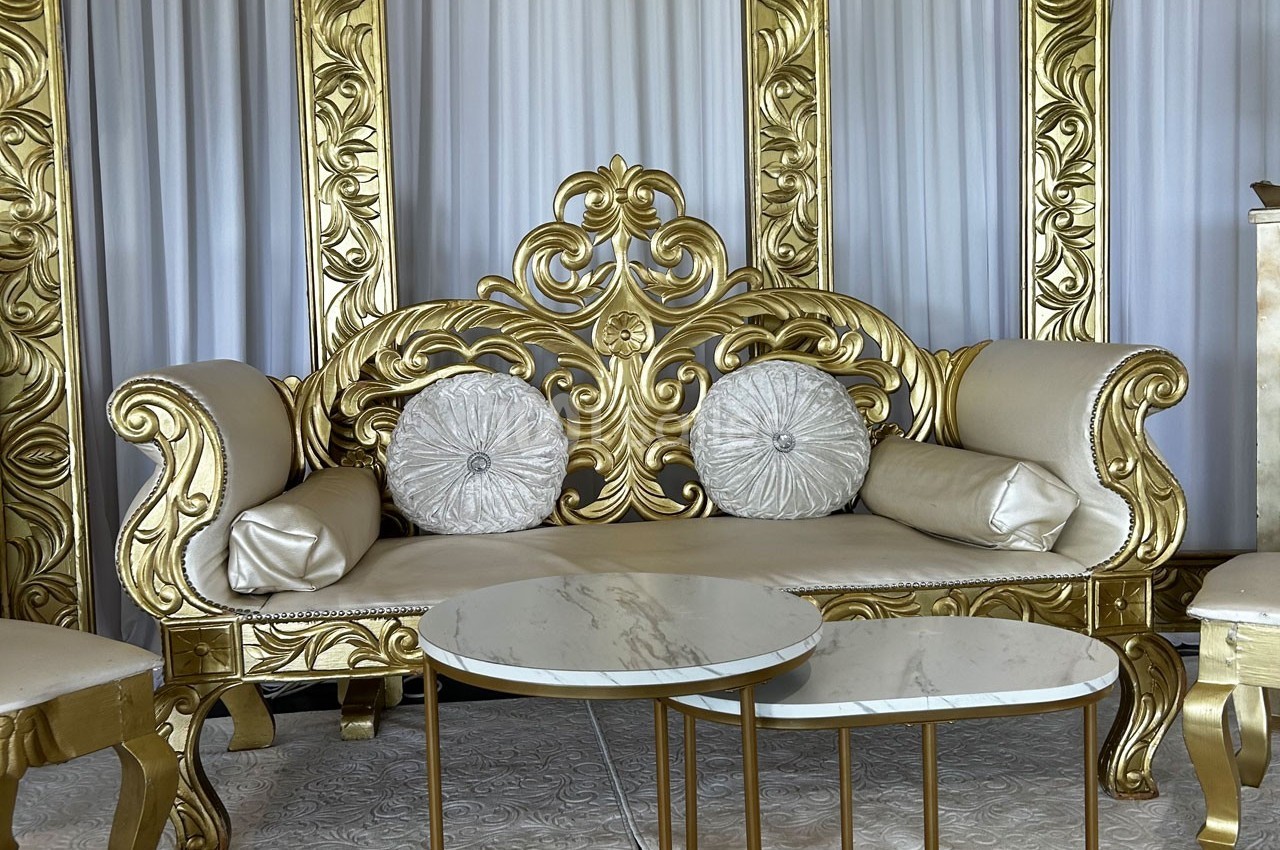 Canapé doré orné de motifs baroques, accompagné de coussins décoratifs et de tables basses en marbre blanc.