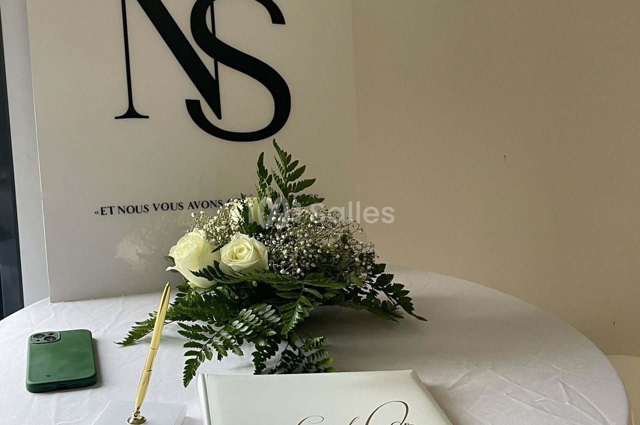 Bouquet de fleurs blanches, livre d'or, stylo doré et smartphone sur une table ronde blanche.