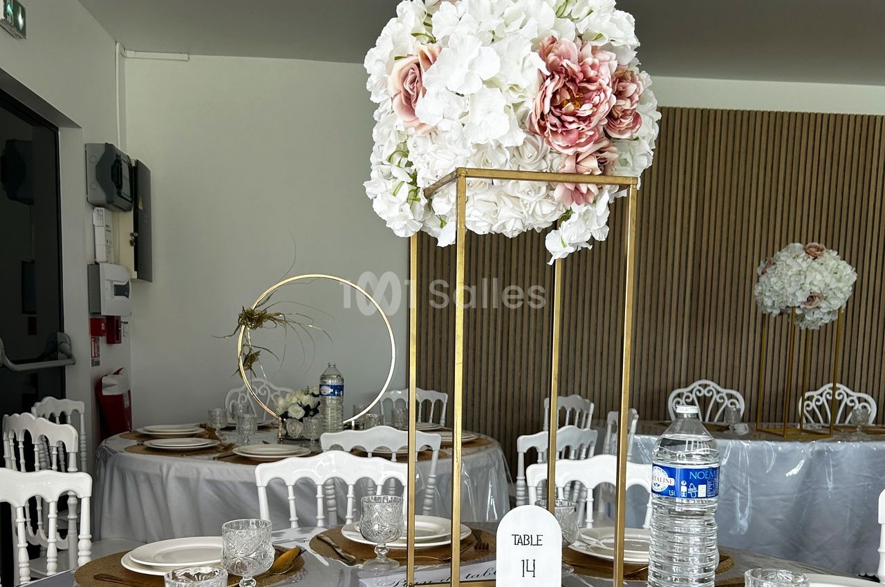 Centre de table floral avec des fleurs blanches et roses sur une structure dorée, entouré de vaisselle élégante.