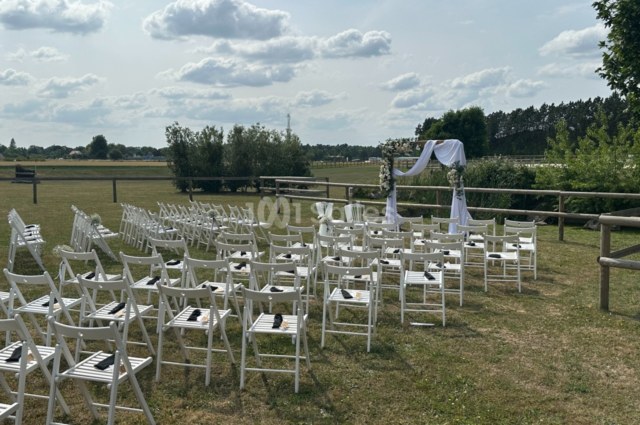 Chaises blanches disposées en rangées devant une arche décorée, installées en extérieur sur une pelouse par temps ensoleillé.