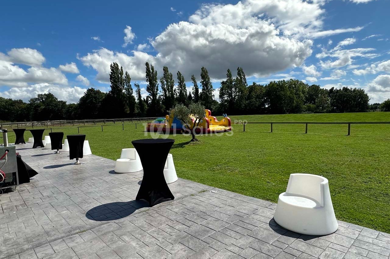 Espace extérieur avec pelouse, mobilier de réception et structure gonflable colorée sous un ciel partiellement nuageux.