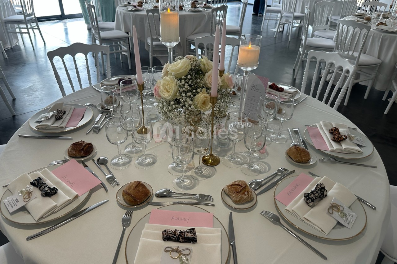 Table de réception élégamment dressée avec des fleurs, bougies, menus et couverts disposés autour d'assiettes.