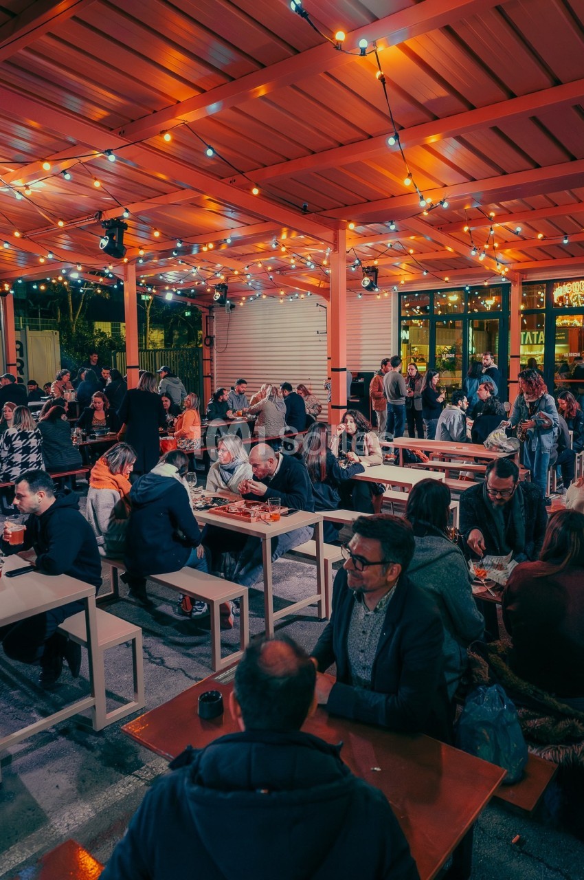 Terrasse animée en soirée avec des tables remplies de personnes partageant un repas sous des guirlandes lumineuses.
