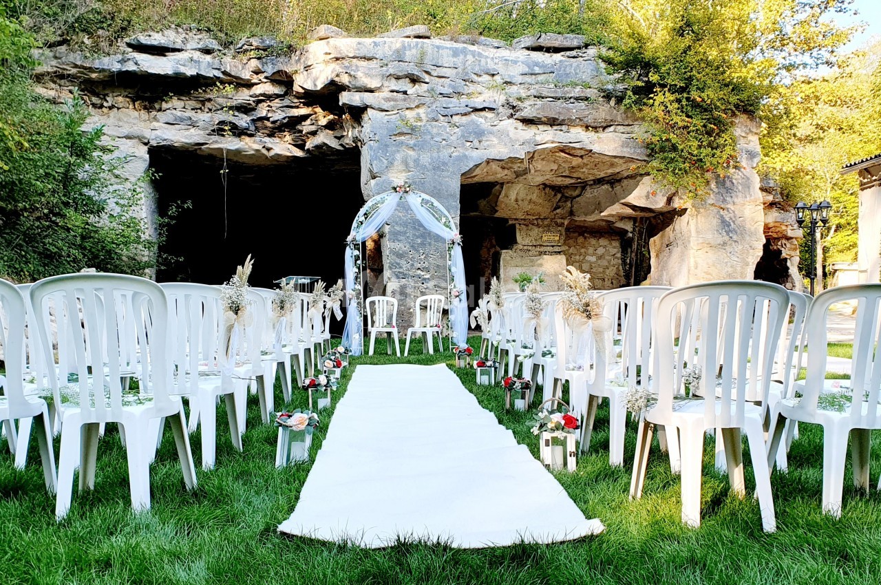 Allée centrale décorée pour une cérémonie de mariage en plein air, entourée de chaises blanches et d'une arche florale.