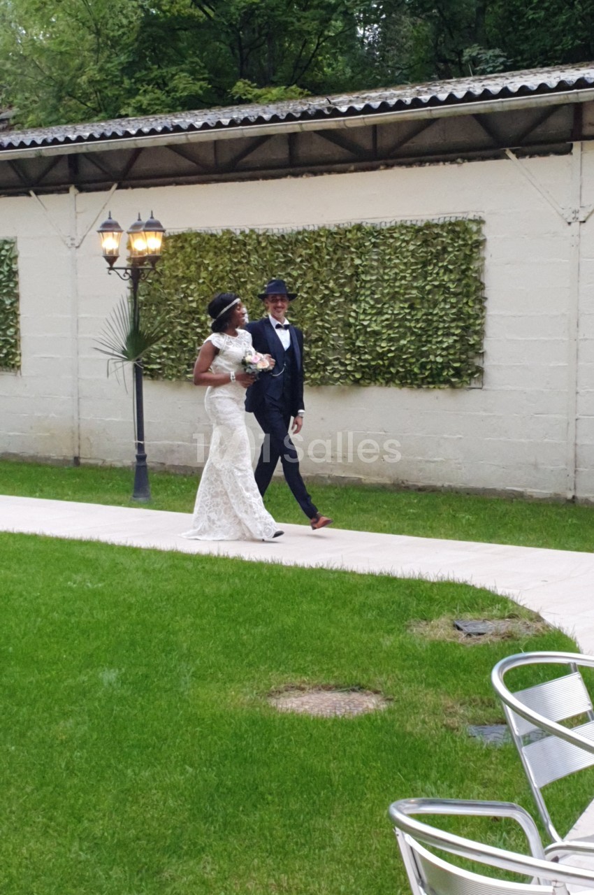 Un couple marche sur une allée pavée dans un jardin, la mariée en robe blanche tenant un bouquet.
