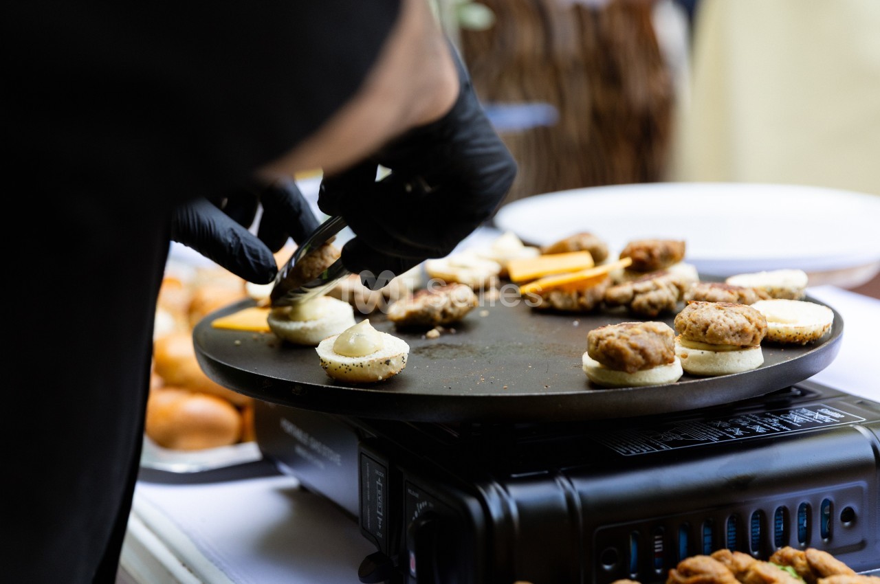 Un cuisinier en gants noirs prépare des amuse-bouches sur une plaque chauffante lors d'un événement.