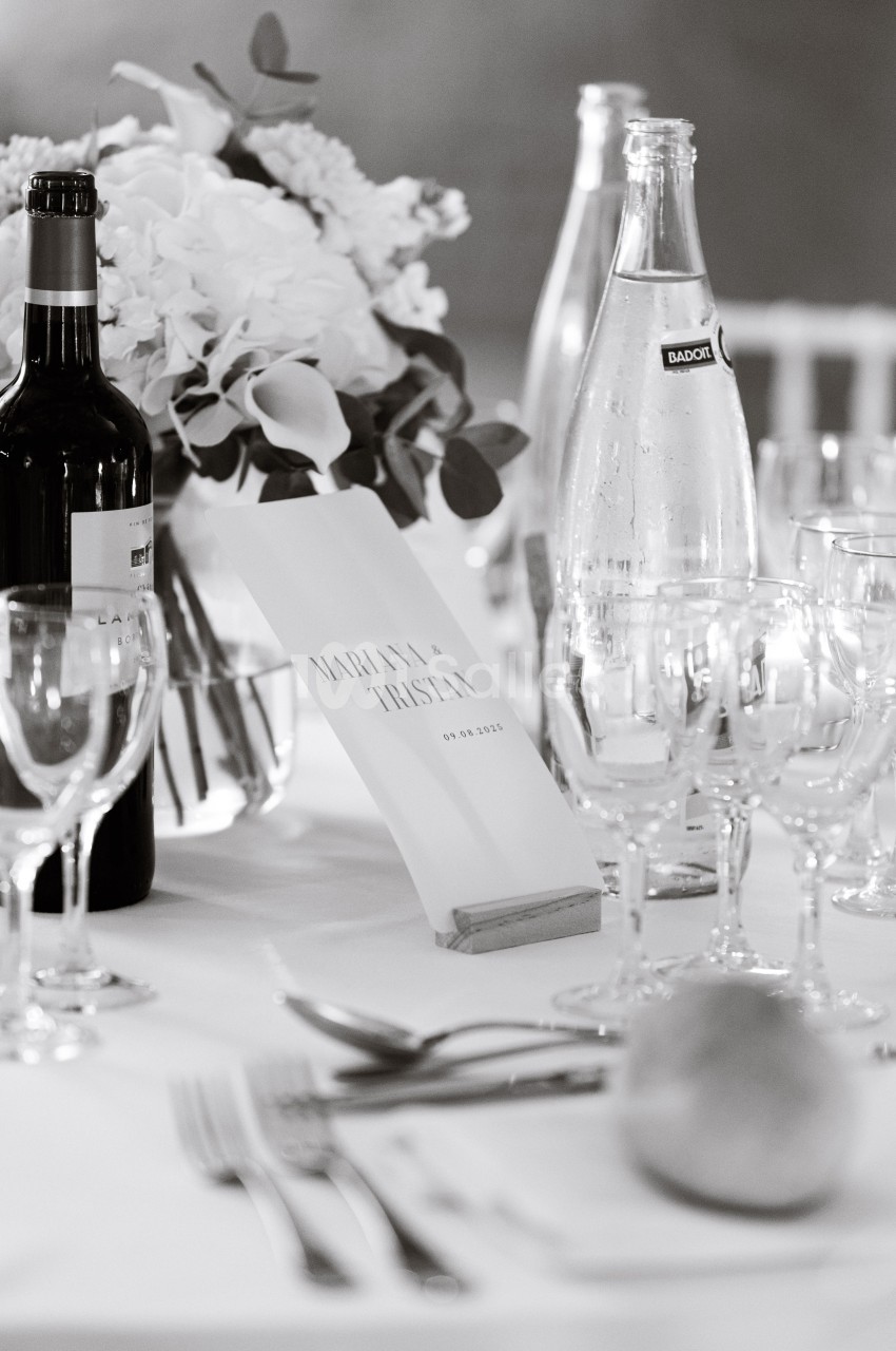 Table de réception élégamment dressée avec fleurs, bouteilles, verres et un menu portant des prénoms et une date.