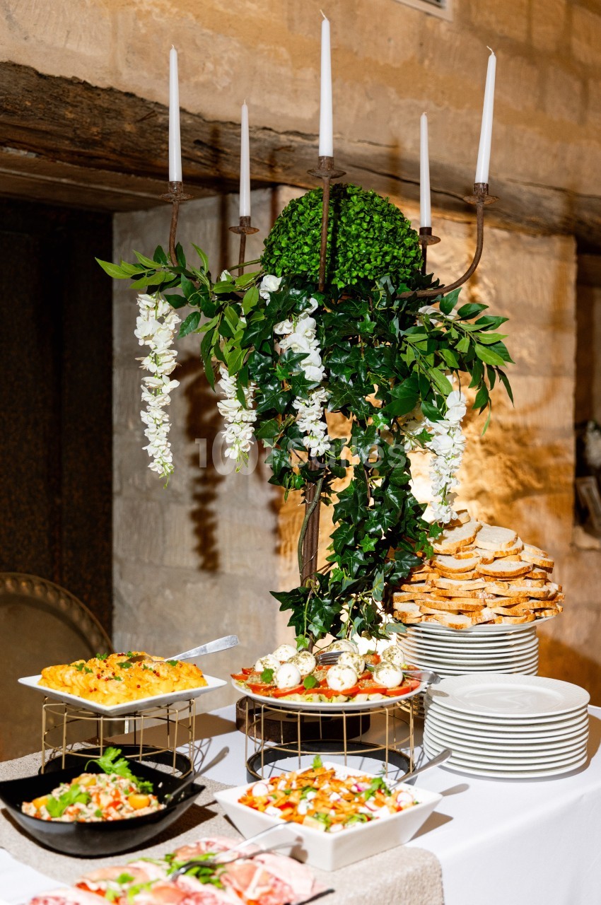 Buffet décoré avec des bougies, des plantes et des plats variés, comprenant tartes, salades et assiettes de pain empilé.