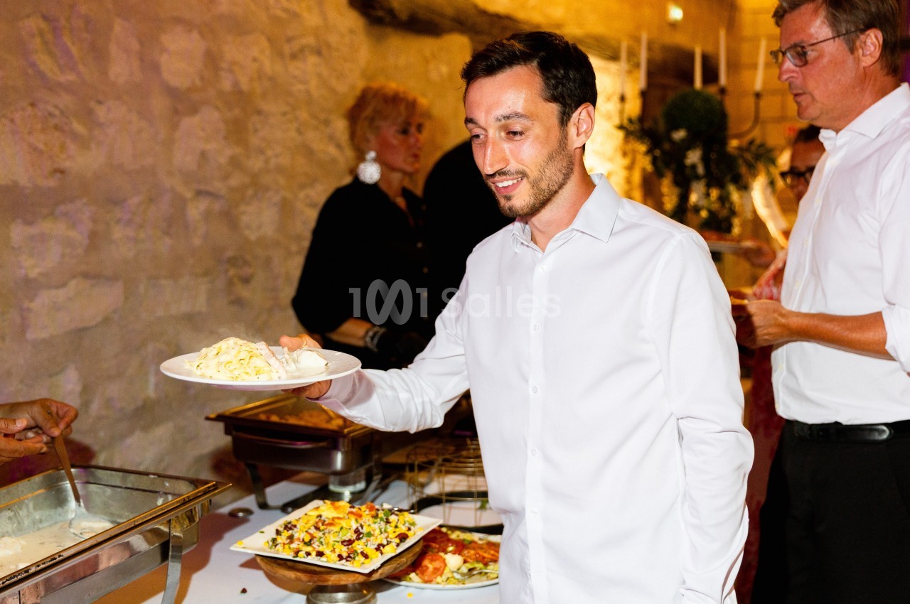 Un homme en chemise blanche se sert un plat lors d'un buffet dans un cadre intérieur éclairé.