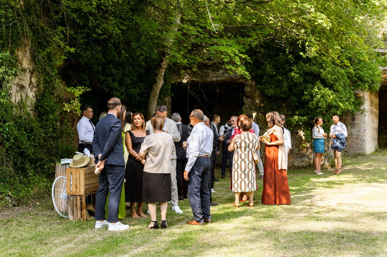 Un groupe de personnes discute dans un jardin ombragé, près d'une table en bois et d'une végétation dense.