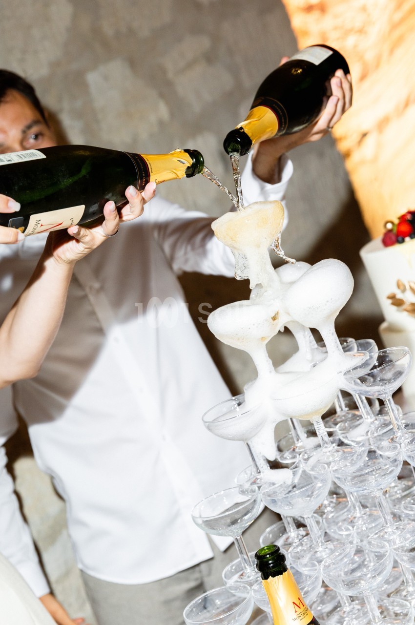 Deux bouteilles de champagne versent simultanément du vin dans une pyramide de coupes en verre.