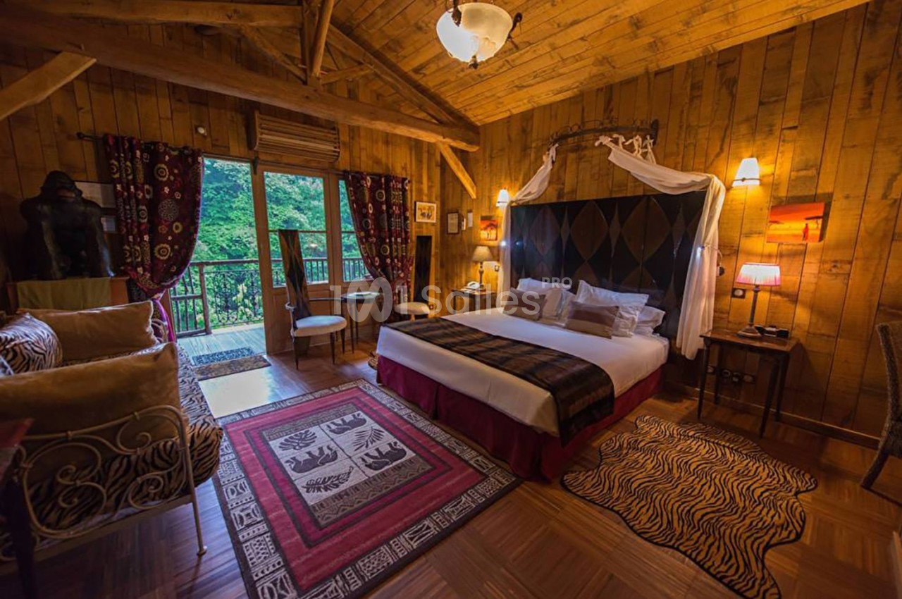 Chambre en bois chaleureuse avec lit double, tapis décoratifs, fauteuils, et vue sur une forêt par une porte-fenêtre.