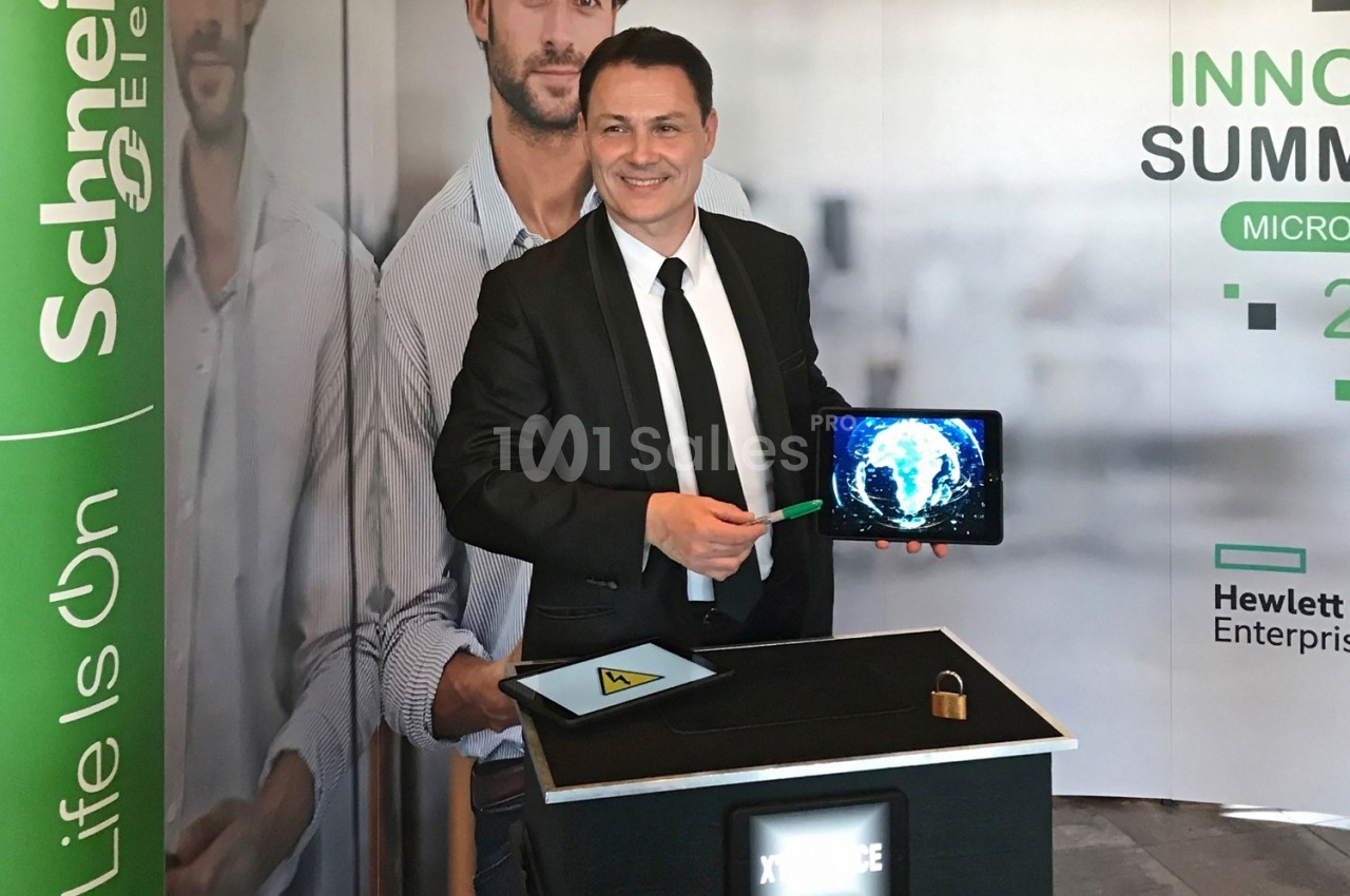 Un homme souriant présente une tablette affichant un globe lumineux, debout devant un stand d'exposition.