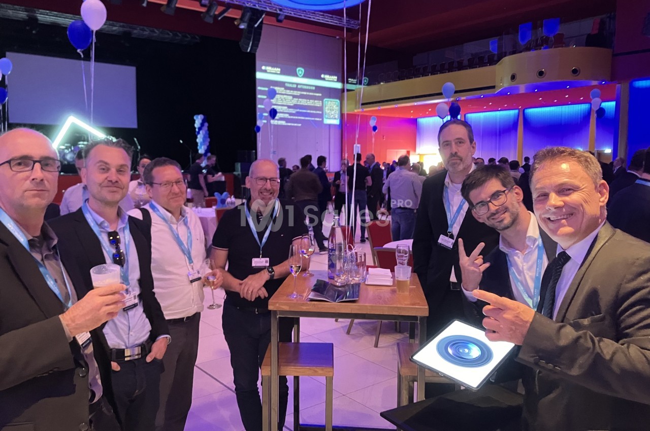 Groupe d'hommes en tenue professionnelle discutant autour de tables hautes lors d'un événement en intérieur.