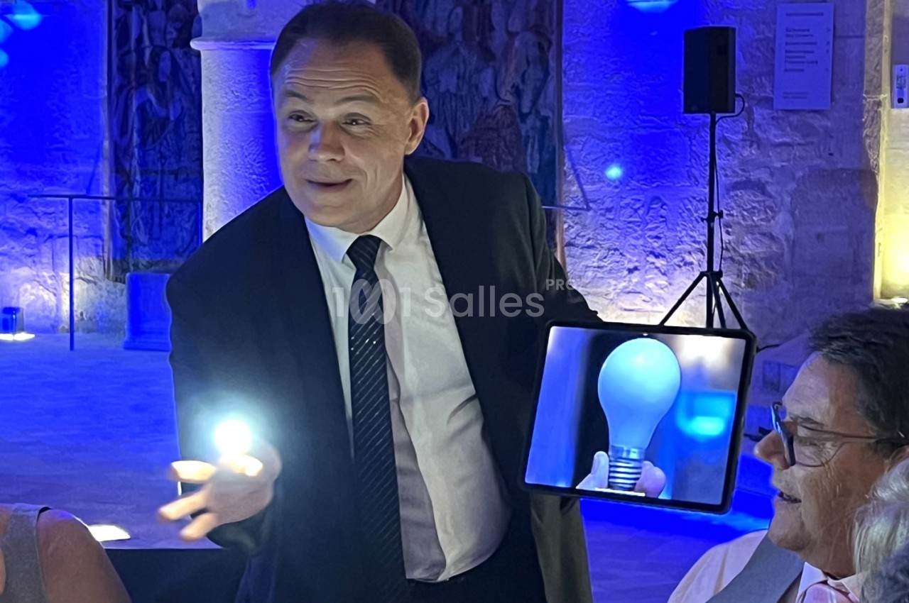 Un homme en costume tient une lumière dans sa main et montre une tablette affichant une ampoule, dans un cadre lumineux.
