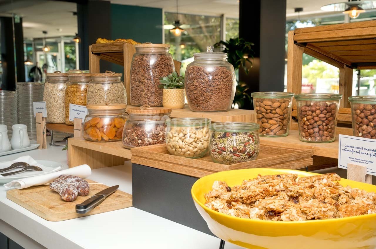 Buffet de petit-déjeuner avec céréales, fruits secs, noix et granola présentés dans des bocaux en verre et un saladier.