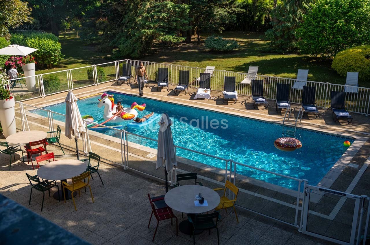 Piscine extérieure entourée de chaises longues, tables et chaises colorées, avec des jouets gonflables dans l'eau.