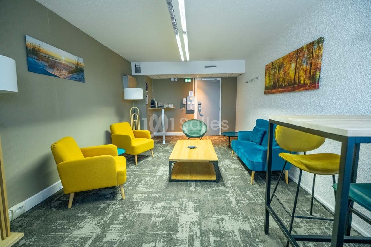 Salle de détente avec fauteuils colorés, table basse en bois, tapis gris et décorations murales.
