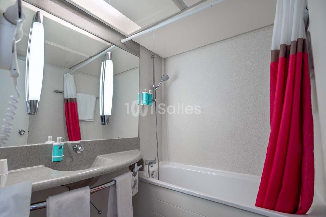 Salle de bain avec lavabo, miroir, baignoire, douchette murale et rideau rouge et blanc.