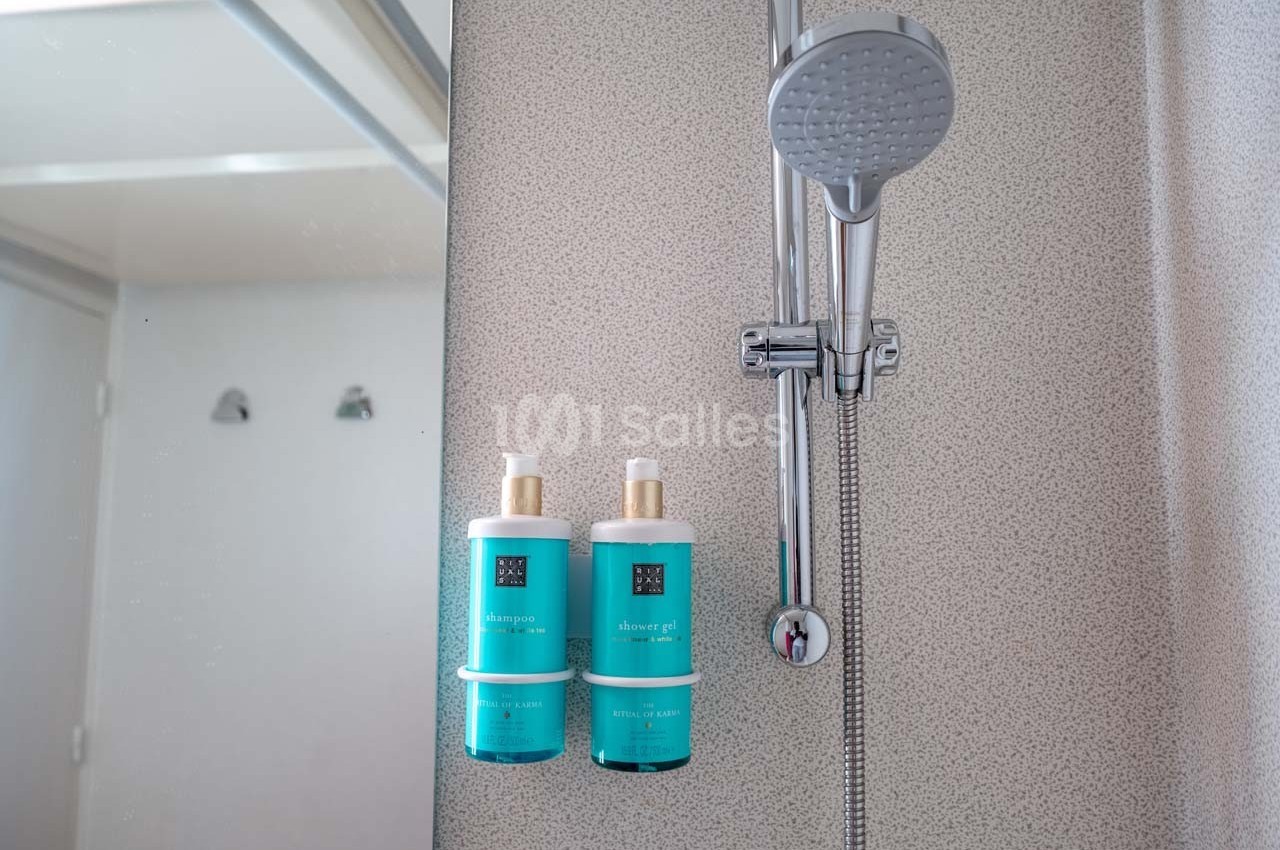 Deux flacons de shampooing et gel douche turquoise fixés à un support mural dans une cabine de douche moderne.