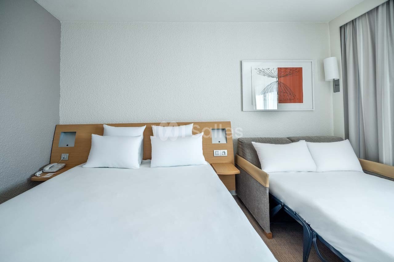 Chambre d'hôtel avec un lit double, un canapé-lit, des draps blancs et un tableau encadré sur le mur.