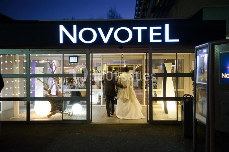 Entrée d'un hôtel Novotel en soirée, avec un couple en tenue de mariage entrant dans le bâtiment éclairé.