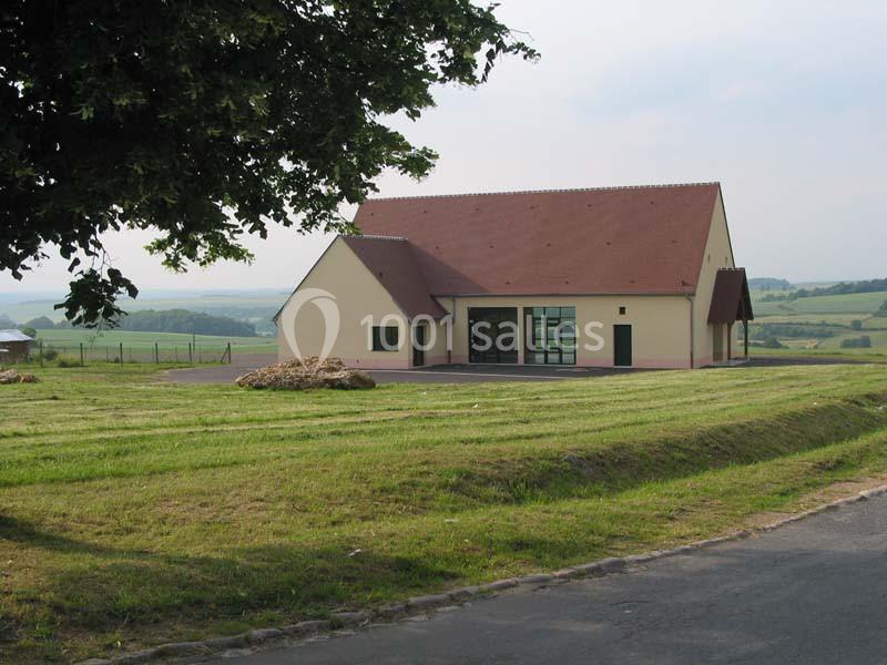 Bâtiment à toit rouge entouré de pelouses, situé dans un paysage rural avec collines en arrière-plan.
