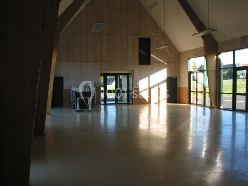 Intérieur d'une grande salle lumineuse avec des murs en bois, un sol clair et des ouvertures vitrées donnant sur l'extérieur.